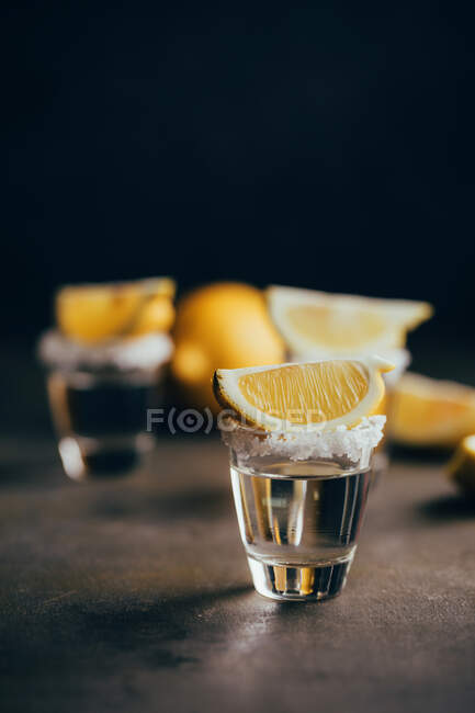 Tequila shots with salt and lemon placed on reflective surface against dark background — Stock Photo