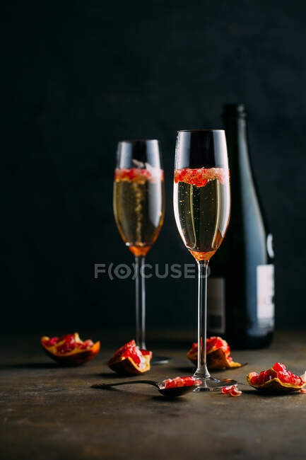 Coquetel de champanhe com romã colocado na superfície rústica contra fundo escuro — Fotografia de Stock