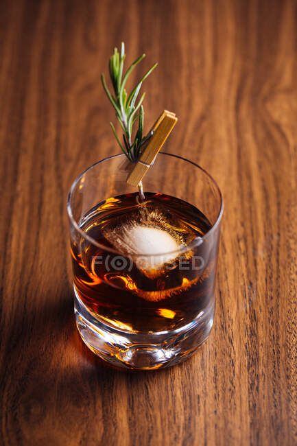 Glass of whiskey with rosemary placed on wooden table — Stock Photo