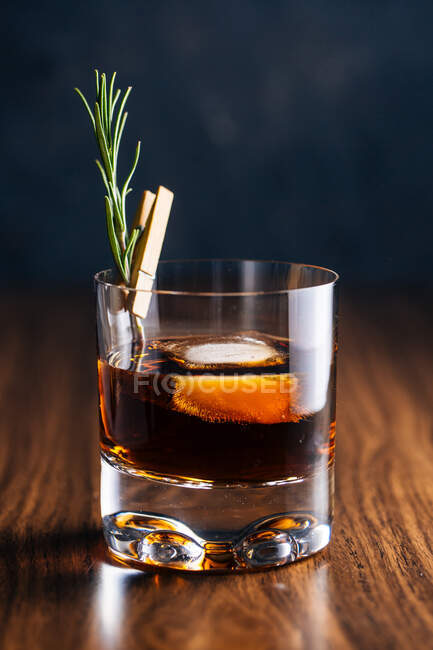 Vaso de whisky con romero colocado sobre mesa de madera - foto de stock