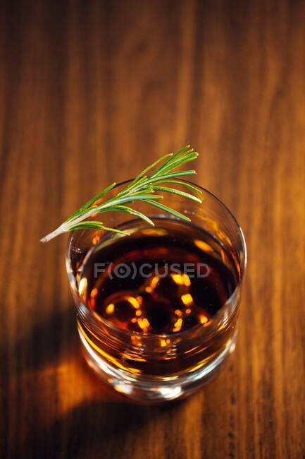 Copo de uísque com alecrim colocado sobre mesa de madeira — Fotografia de Stock