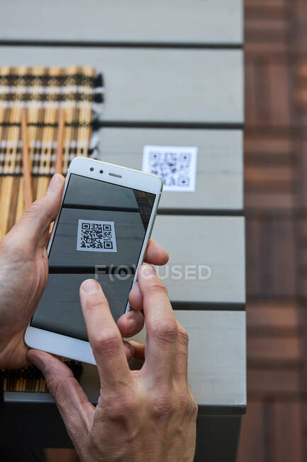 From above of crop unrecognizable male using smartphone and scanning QR code of menu of restaurant — Stock Photo