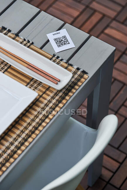 З верху паперу з QR кодом меню, поміщеного на столі з паличками та тарілками в азіатському ресторані. — стокове фото