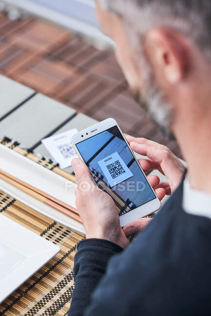 Зверху врожаю невизначений чоловік використовує смартфон і сканує QR-код меню ресторану — стокове фото