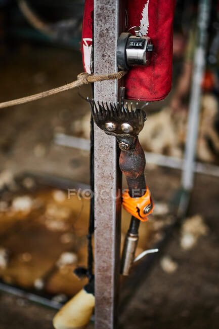 Cortadoras de metal oxidado para esquilar ovejas colgando cerca de viga de metal en el granero en el campo - foto de stock