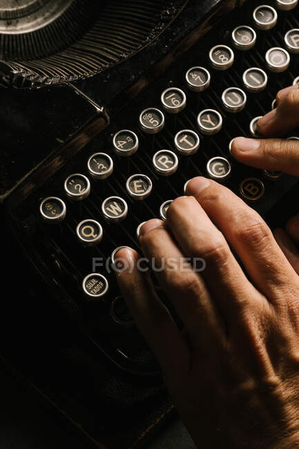 De arriba tiro de las manos de la persona anónima que escribe en el teclado de la máquina de escribir vintage - foto de stock