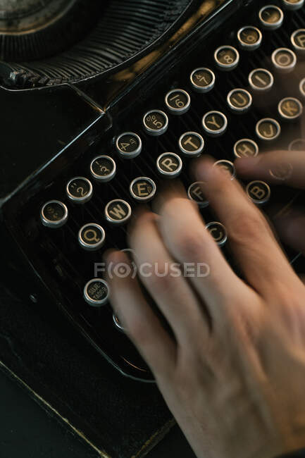 De arriba tiro de las manos de la persona anónima que escribe en el teclado de la máquina de escribir vintage - foto de stock