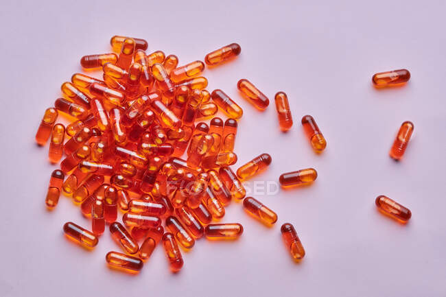 Composición de vista superior de píldoras de color naranja dispersas sobre fondo rosa en estudio de luz - foto de stock