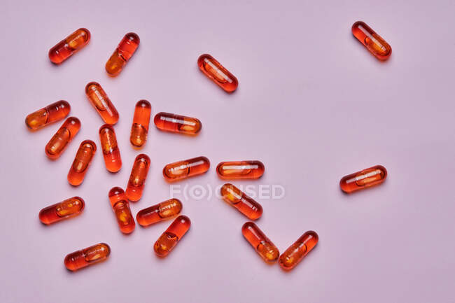 Vista dall'alto composizione di pillole arancioni sparsi su sfondo rosa in studio luce — Foto stock
