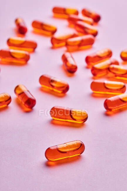 Composition de pilules orange éparpillées sur fond rose en studio lumière — Photo de stock