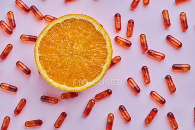 Top view composition of ripe cut oranges arranged on pink surface near scattered pills in light studio — Stock Photo