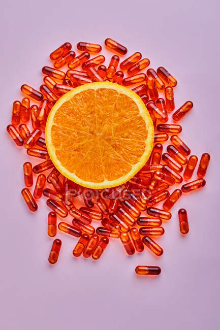 Верхній вид композиції стиглих вирізьблених апельсинів розташованих на рожевій поверхні біля розсіяних пілюль у легкій студії. — стокове фото