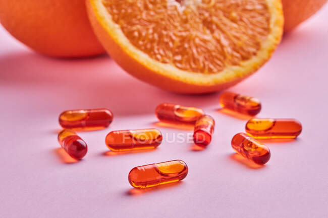 Composition of ripe cut oranges arranged on pink surface near scattered pills in light studio — Stock Photo