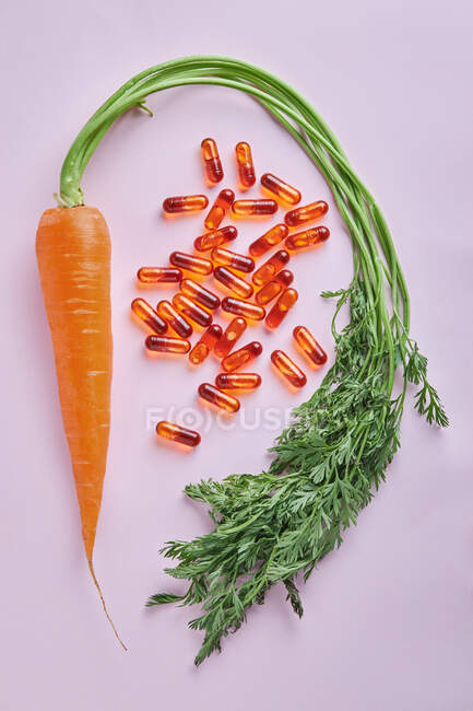 Par dessus la composition de pilules de vitamines dispersées disposées sur une table rose près de carottes mûres — Photo de stock