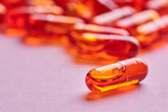 Composition of orange pills scattered on pink background in light studio — Stock Photo