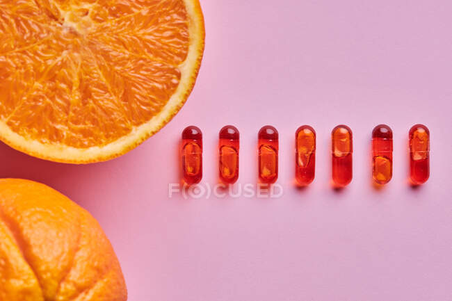 Top view composition of ripe cut oranges arranged on pink surface near row of pills — Stock Photo
