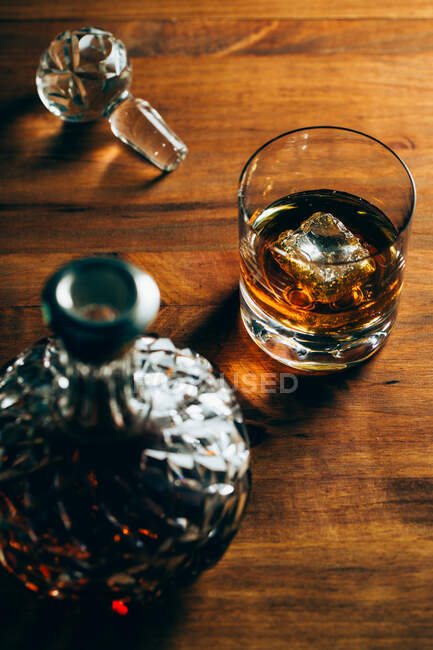 Склянка холодного віскі з льодом, розміщена на дерев'яному столі поруч з деканером на чорному фоні — стокове фото