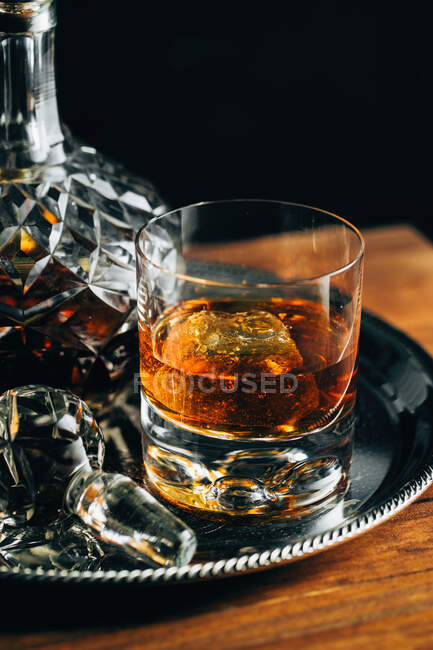 Vidro de uísque frio com gelo colocado na mesa de madeira perto decanter sobre fundo preto — Fotografia de Stock