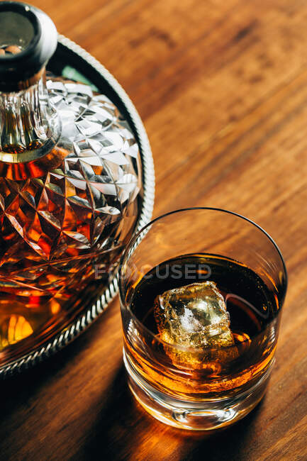 Vidro de uísque frio com gelo colocado na mesa de madeira perto decanter sobre fundo preto — Fotografia de Stock