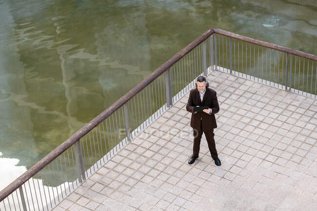 Зверху бородатий чоловік середнього віку в елегантному костюмі, що переглядається на планшеті на терасі — стокове фото