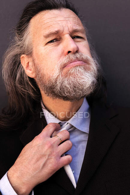 Stressful tired aged gray haired bearded male entrepreneur in formal suit loosening necktie after hardwork — Stock Photo