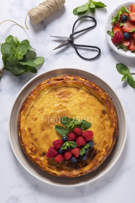 From above view of cheesecake decorated with raspberries, blueberries and mint leaves, placed on marble table — Stock Photo