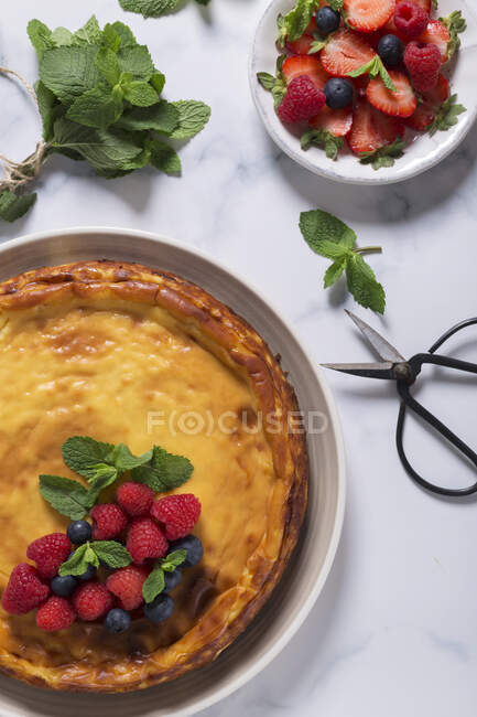 From above view of cheesecake decorated with raspberries, blueberries and mint leaves, placed on marble table — Stock Photo