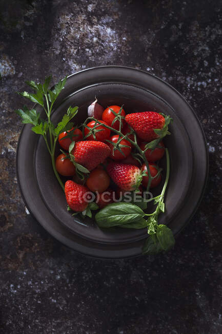 Draufsicht auf Schüssel mit frischen Erdbeeren und Tomaten zur Zubereitung einer Gazpacho-kalten Suppe auf dunklem Tisch — Stockfoto