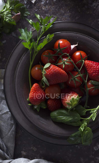 Vista superior da tigela com morango fresco e tomates para preparar uma sopa fria de gaspacho colocada na mesa escura — Fotografia de Stock