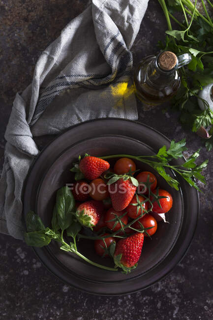 Draufsicht auf Schüssel mit frischen Erdbeeren und Tomaten zur Zubereitung einer Gazpacho-kalten Suppe auf dunklem Tisch — Stockfoto