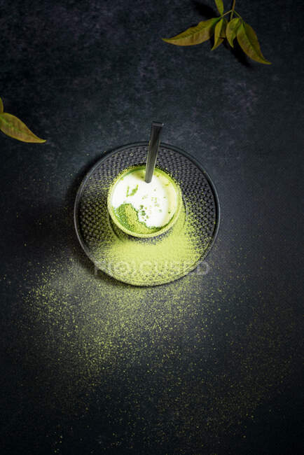 High angle of glass with cold green matcha latte with milk served with straw on saucer on black table — Stock Photo