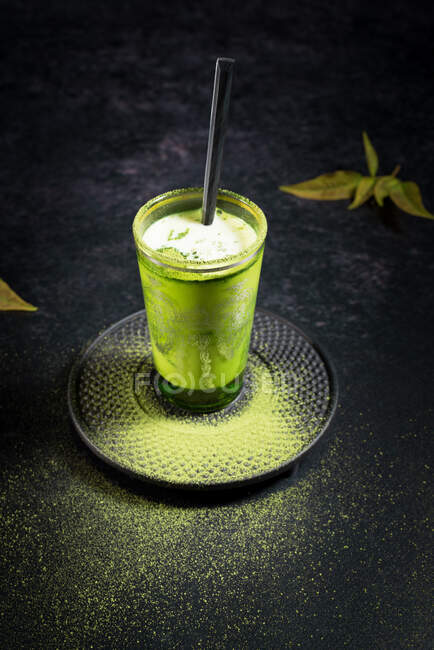 Hoher Glaswinkel mit kaltem grünen Matcha Latte mit Milch serviert mit Stroh auf Untertasse auf schwarzem Tisch — Stockfoto