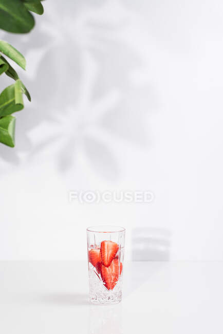 Desintoxicação refrescante saudável infundiu água com morangos maduros fatiados servidos em vidro transparente contra a parede branca com sombras — Fotografia de Stock
