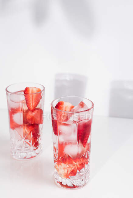 Boisson estivale rafraîchissante avec des fraises fraîches tranchées et des glaçons avec de l'eau servie dans des verres sur une table blanche — Photo de stock