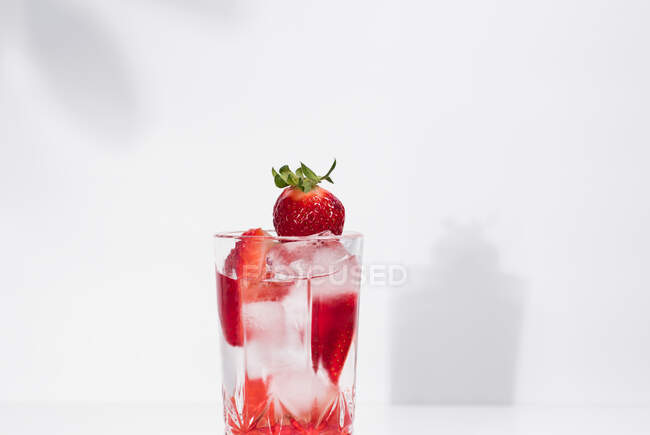 Gesundes, erfrischendes Entgiftungswasser mit frischen reifen Erdbeeren in Scheiben, serviert in transparentem Glas vor weißer Wand mit Schatten — Stockfoto