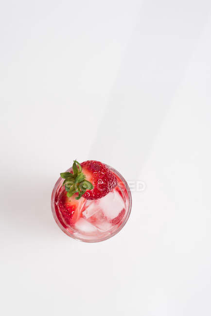 Agua sana y refrescante infundida de desintoxicación con fresas frescas en rodajas maduras servidas en vidrio transparente contra mesa blanca - foto de stock