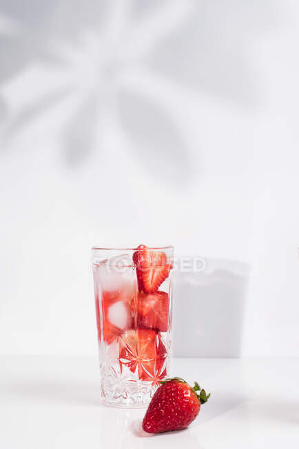 Healthy refreshing detox infused water with fresh ripe sliced strawberries served in transparent glass against white wall with shadows — Stock Photo