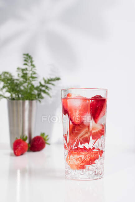 Bebida refrescante de verão com morangos fatiados frescos e cubos de gelo com água servida em vidro sobre mesa branca — Fotografia de Stock