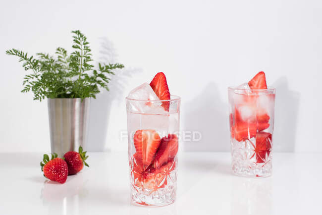 Erfrischendes Sommergetränk mit frischen Erdbeeren und Eiswürfeln mit Wasser in Gläsern auf weißem Tisch — Stockfoto