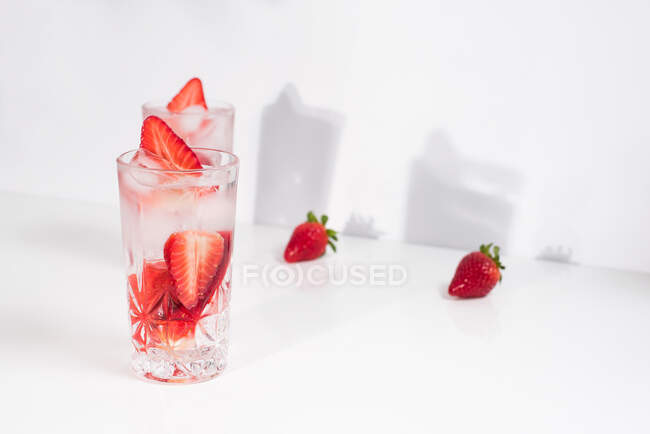 Gesundes, erfrischendes Entgiftungswasser mit frischen reifen Erdbeeren in Scheiben, serviert in transparenten Gläsern vor weißer Wand mit Schatten — Stockfoto