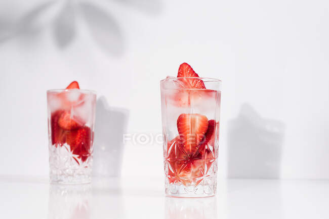 Bevanda estiva rinfrescante con fragole fresche a fette e cubetti di ghiaccio con acqua servita in bicchieri sul tavolo bianco — Foto stock