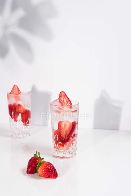 Освіжаючий літній напій зі свіжою нарізаною полуницею та кубиками льоду з водою, поданою в окулярах на білому столі — стокове фото