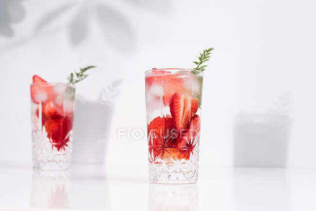 Освіжаючий літній напій зі свіжою нарізаною полуницею та кубиками льоду з водою, поданою в окулярах на білому столі — стокове фото