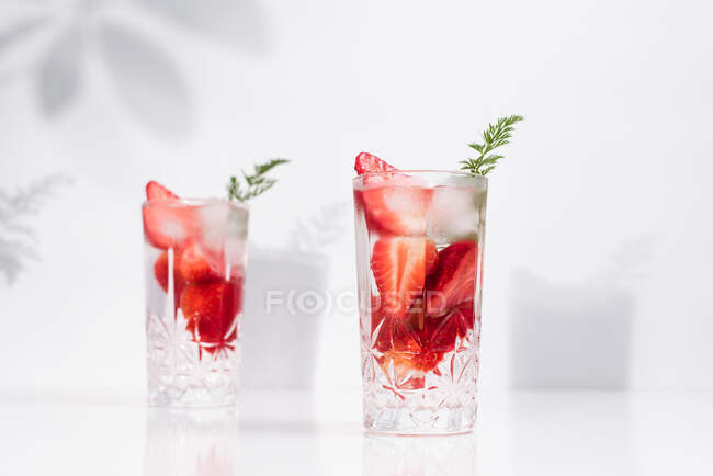 Bebida refrescante de verão com morangos fatiados frescos e cubos de gelo com água servida em copos na mesa branca — Fotografia de Stock