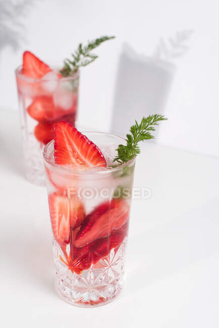 Bevanda estiva rinfrescante con fragole fresche a fette e cubetti di ghiaccio con acqua servita in bicchieri sul tavolo bianco — Foto stock