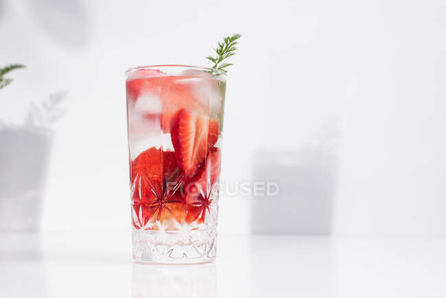 Gesundes, erfrischendes Entgiftungswasser mit frischen reifen Erdbeeren in Scheiben, serviert in transparentem Glas vor weißer Wand mit Schatten — Stockfoto
