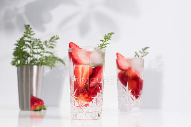 Erfrischendes Sommergetränk mit frischen Erdbeeren und Eiswürfeln mit Wasser in Gläsern auf weißem Tisch — Stockfoto