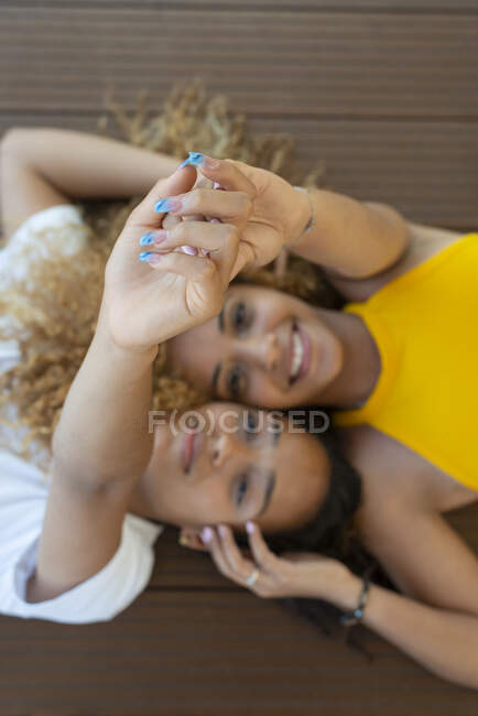 Top view of delighted African American female friends lying face to face on wooden floor — Stock Photo