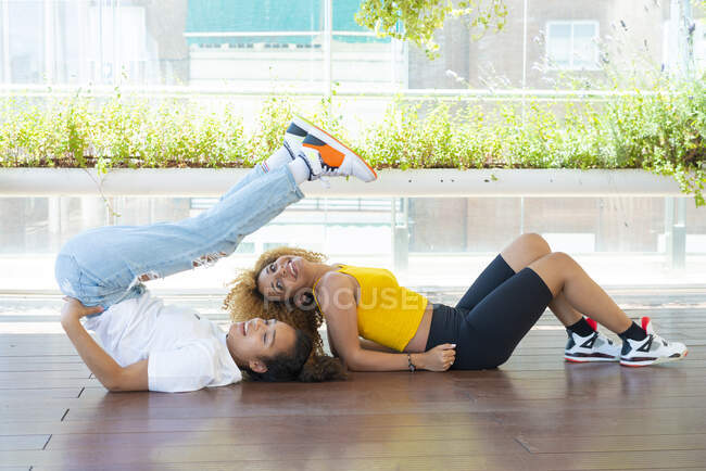 Вид сбоку на лучших афроамериканских подруг, лежащих на деревянном полу на веранде и веселящихся вместе — стоковое фото