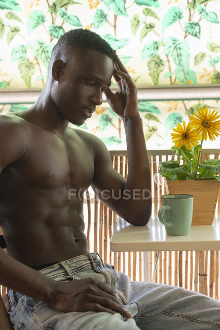 Vista lateral do homem afro-americano pensativo sem camisa mostrando músculos em casa e olhando para longe — Fotografia de Stock